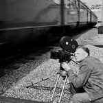849528 Afbeelding van cineast Herman Wassenaar tijdens het filmen van treinen bij de spoorbrug over het ...